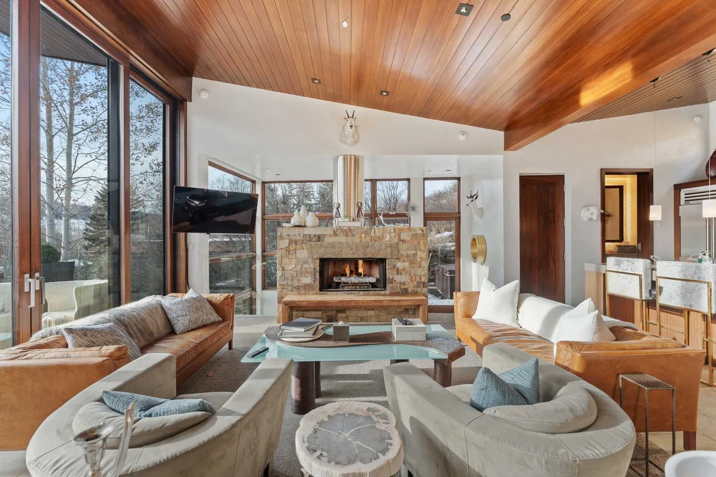 A bright living room with seating arranged around a stone fireplace and glass coffee table.