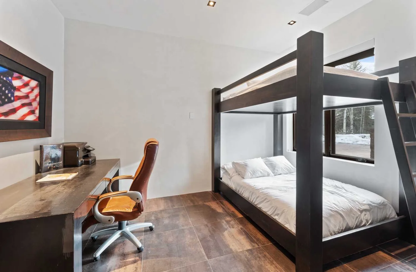 A bedroom with a dark bunk bed, a desk, and a chair.