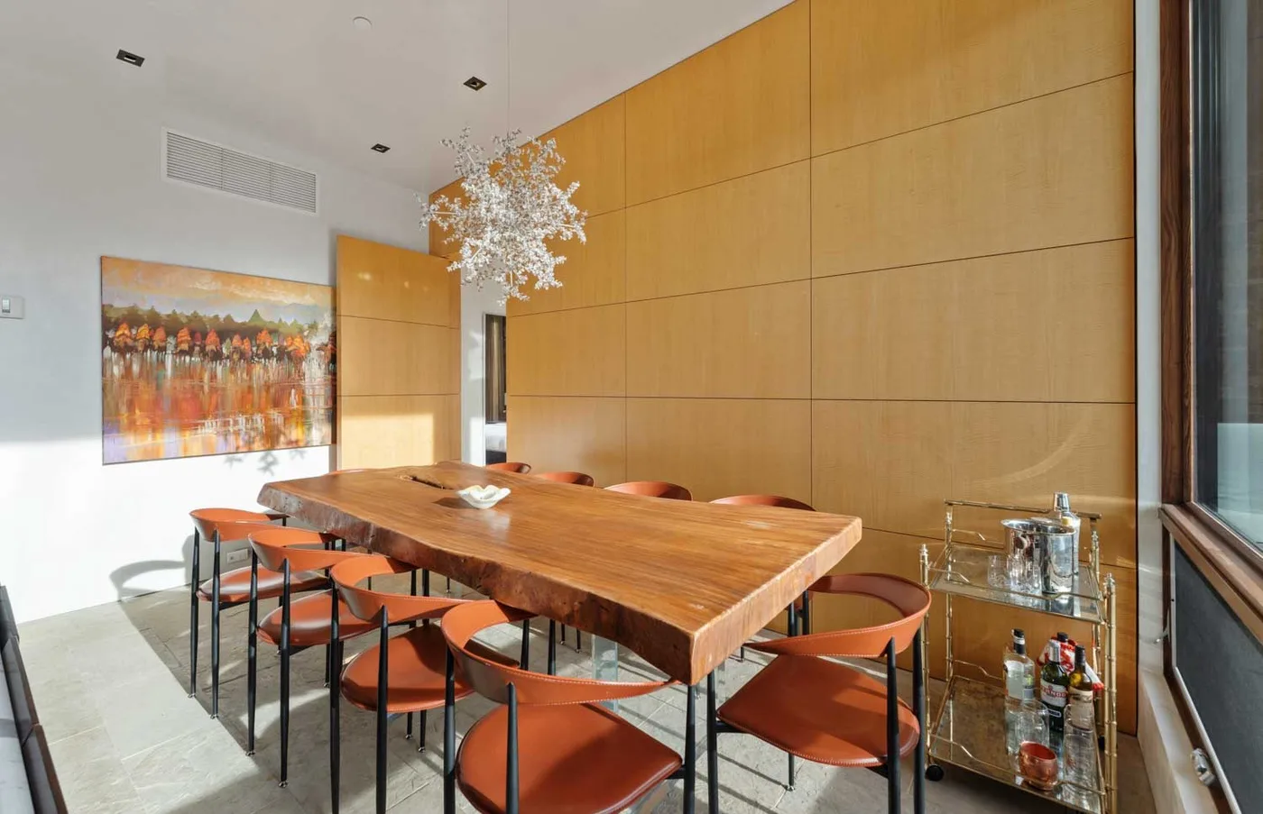 A dining area with a long wooden table, orange seating, and wall art.