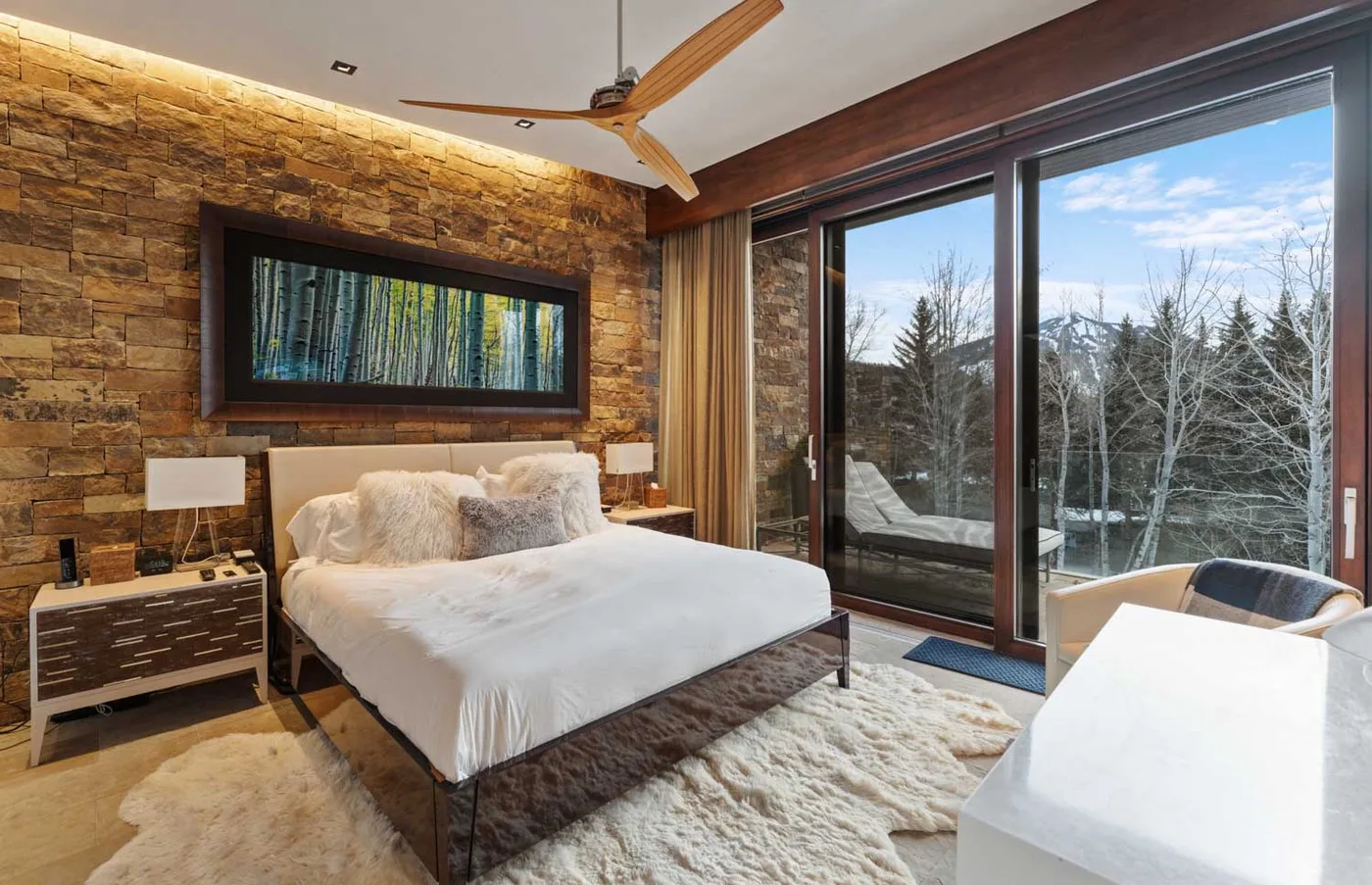 A bedroom with a bed, stone accent wall, and large windows.