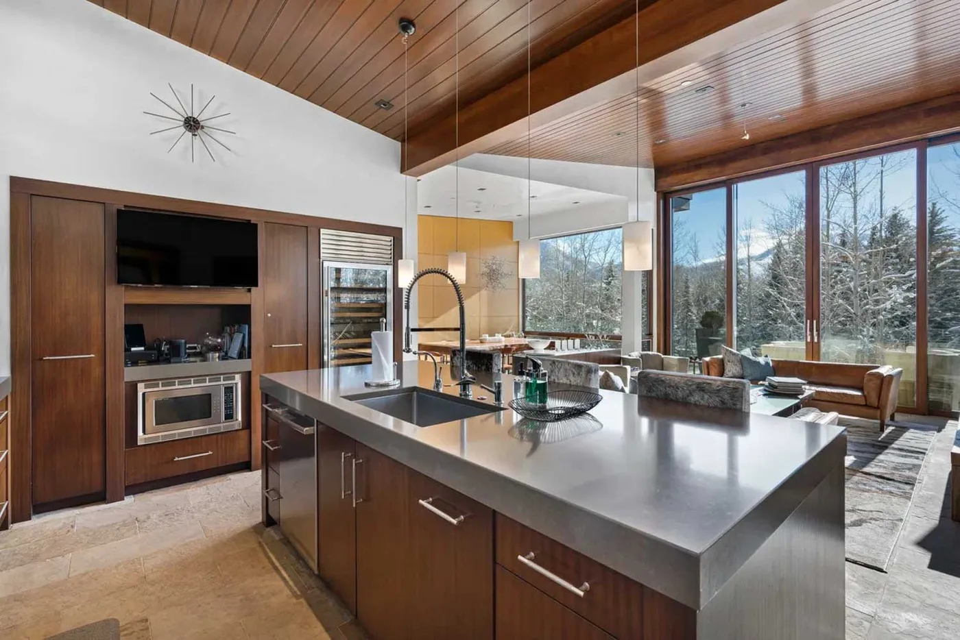 An open-plan kitchen with a large island overlooks a living area and tall windows.