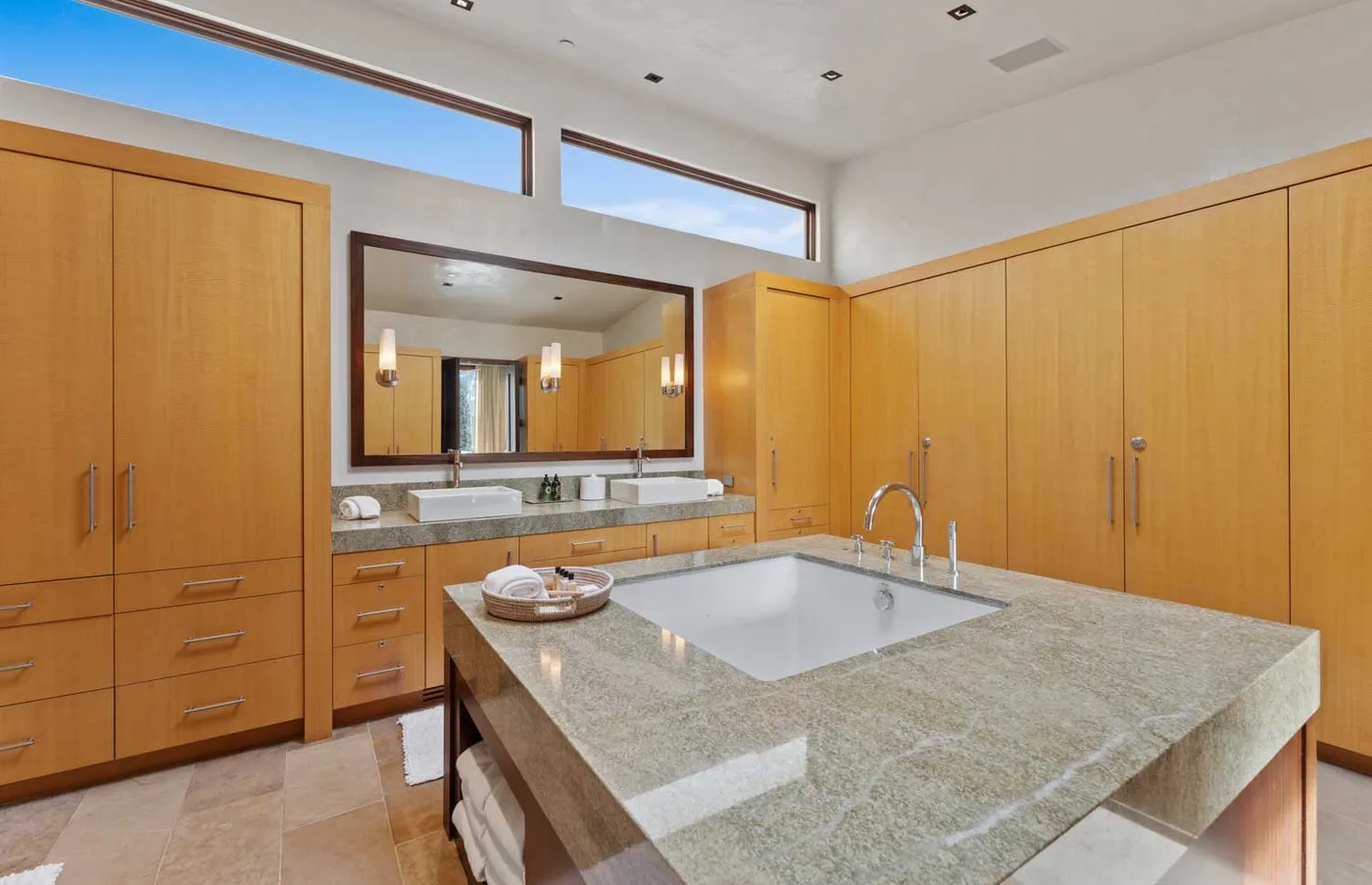 A spacious bathroom with a large stone vanity, sink, and mirrored cabinets.