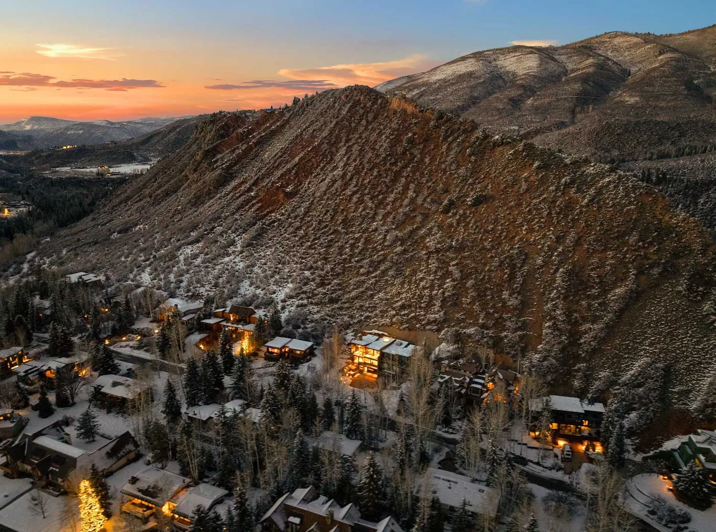 A snow-dusted mountain rises above a cluster of buildings at sunset.