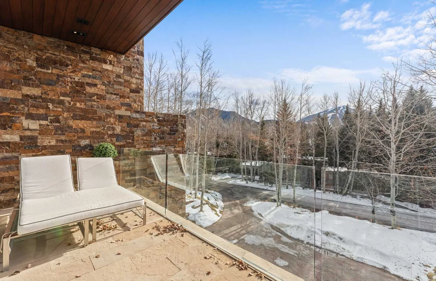 A balcony with outdoor seating overlooks a snowy, tree-lined landscape.