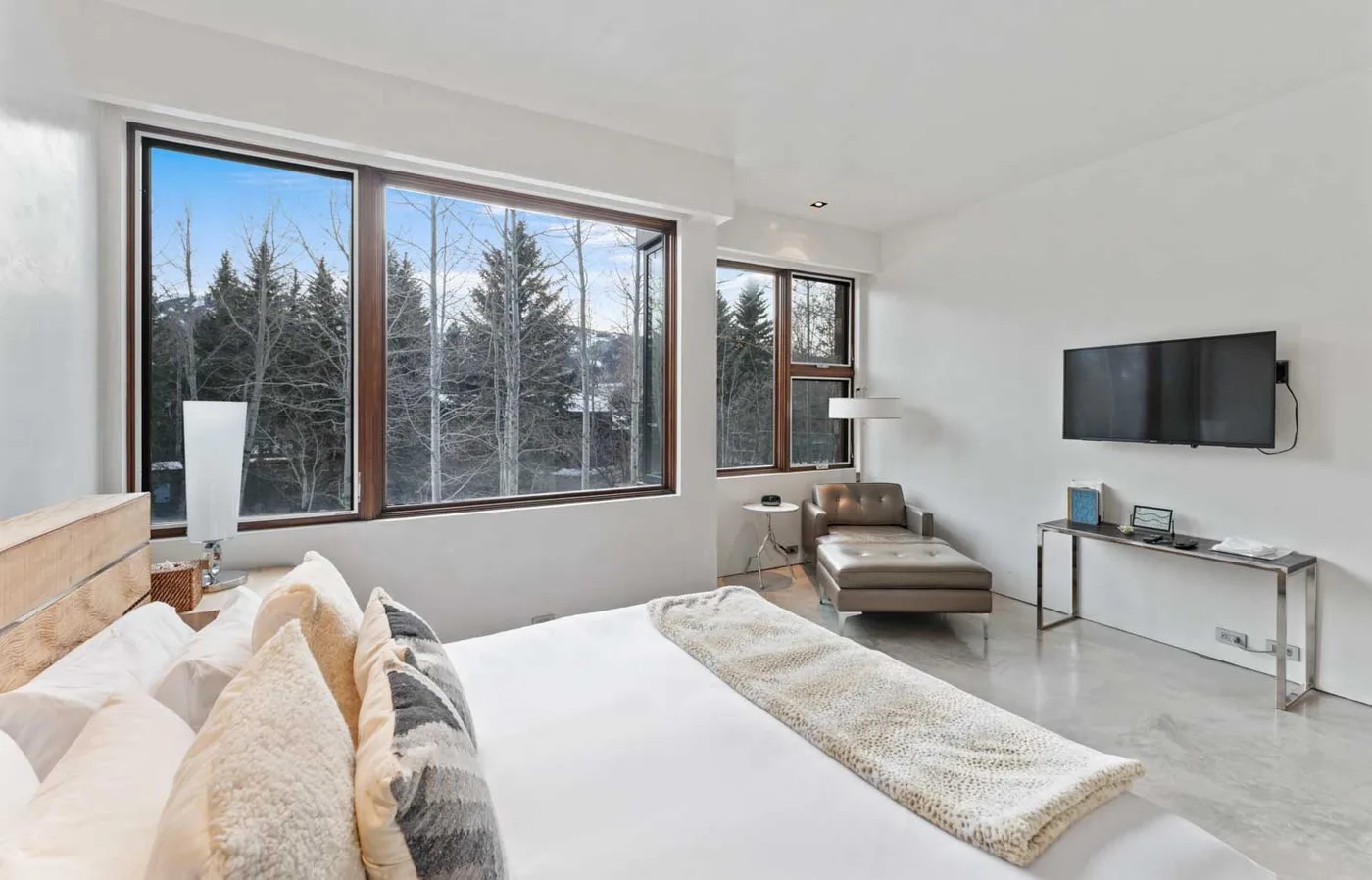 A bright bedroom with a bed, large windows, and a wall-mounted television.