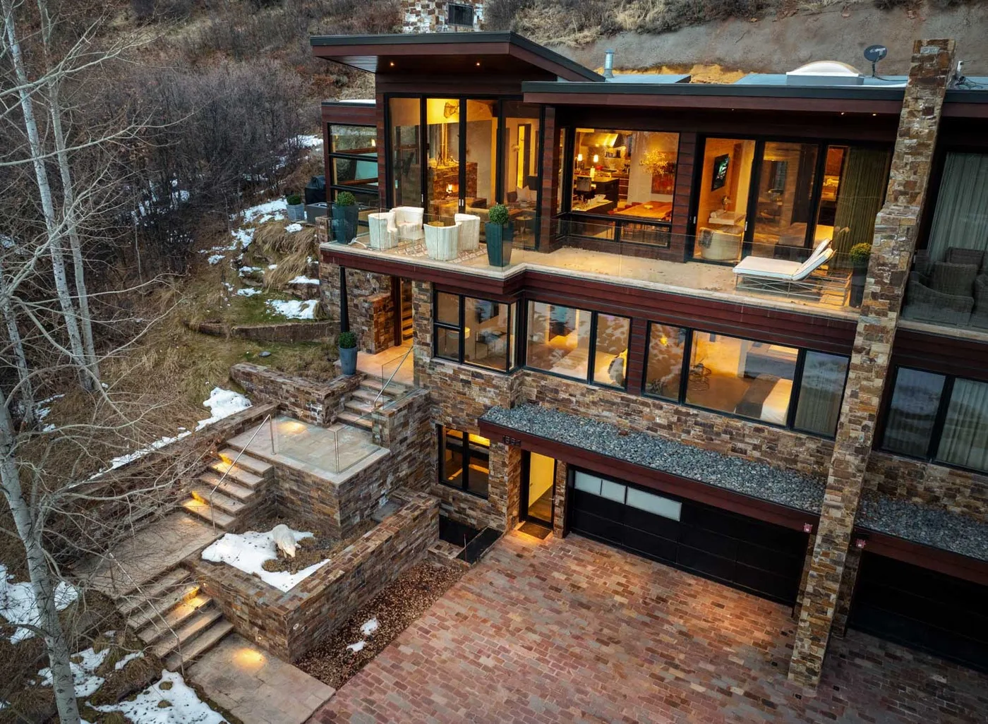 A modern hillside house with broad windows and a stone exterior.