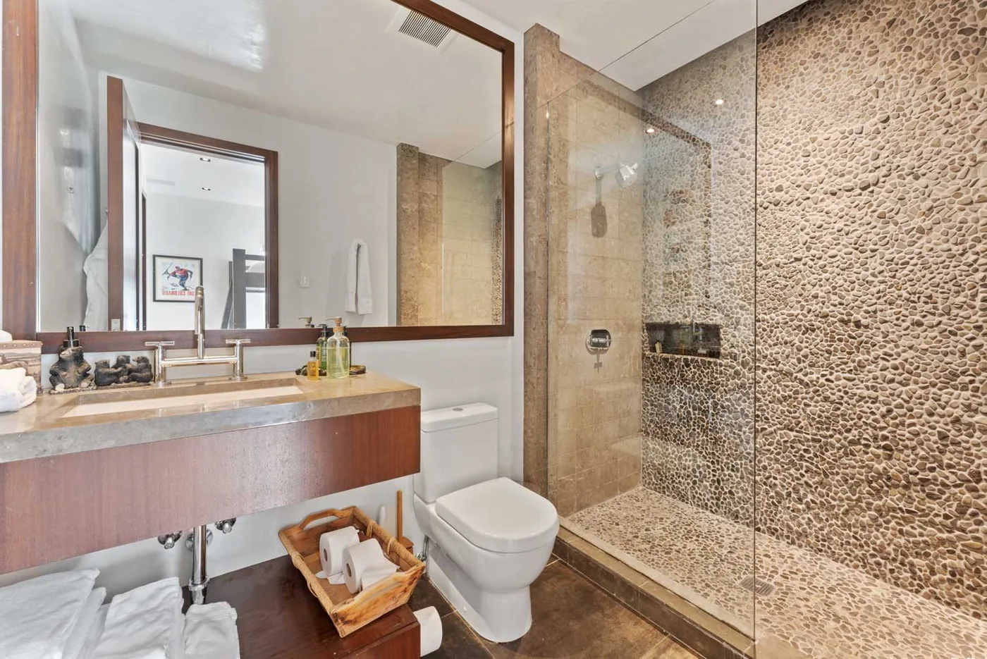A bathroom with a long vanity, mirror, toilet, and glass shower.
