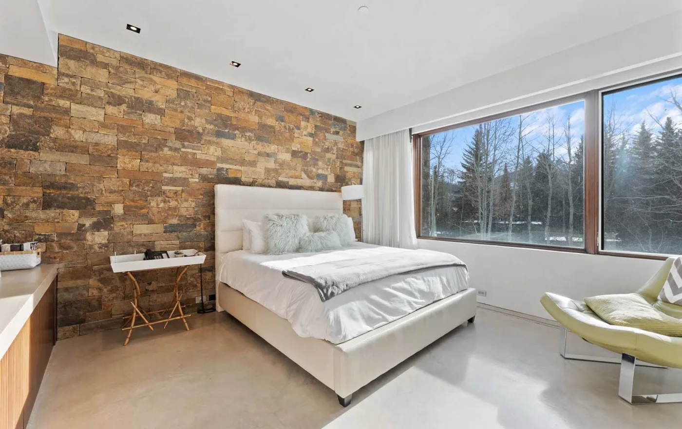 A bedroom with a bed beside large windows overlooking trees.