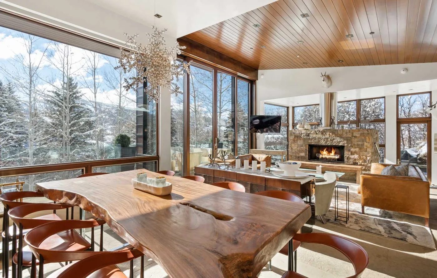 A sunlit dining area with large windows and a stone fireplace.