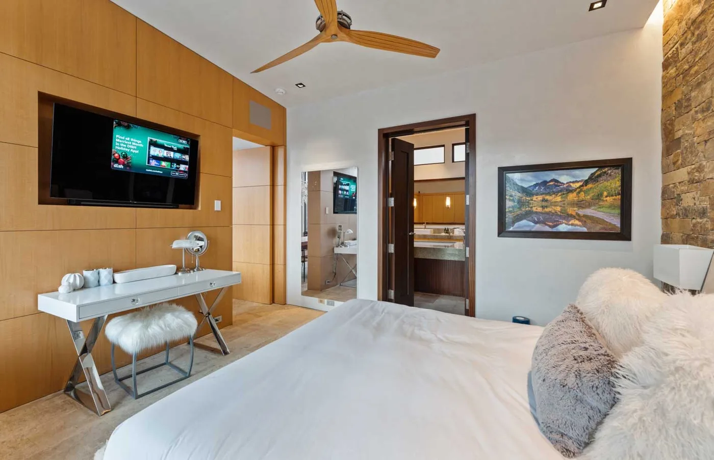 A bedroom with a bed, a wall-mounted television, and a bathroom visible through the doorway.