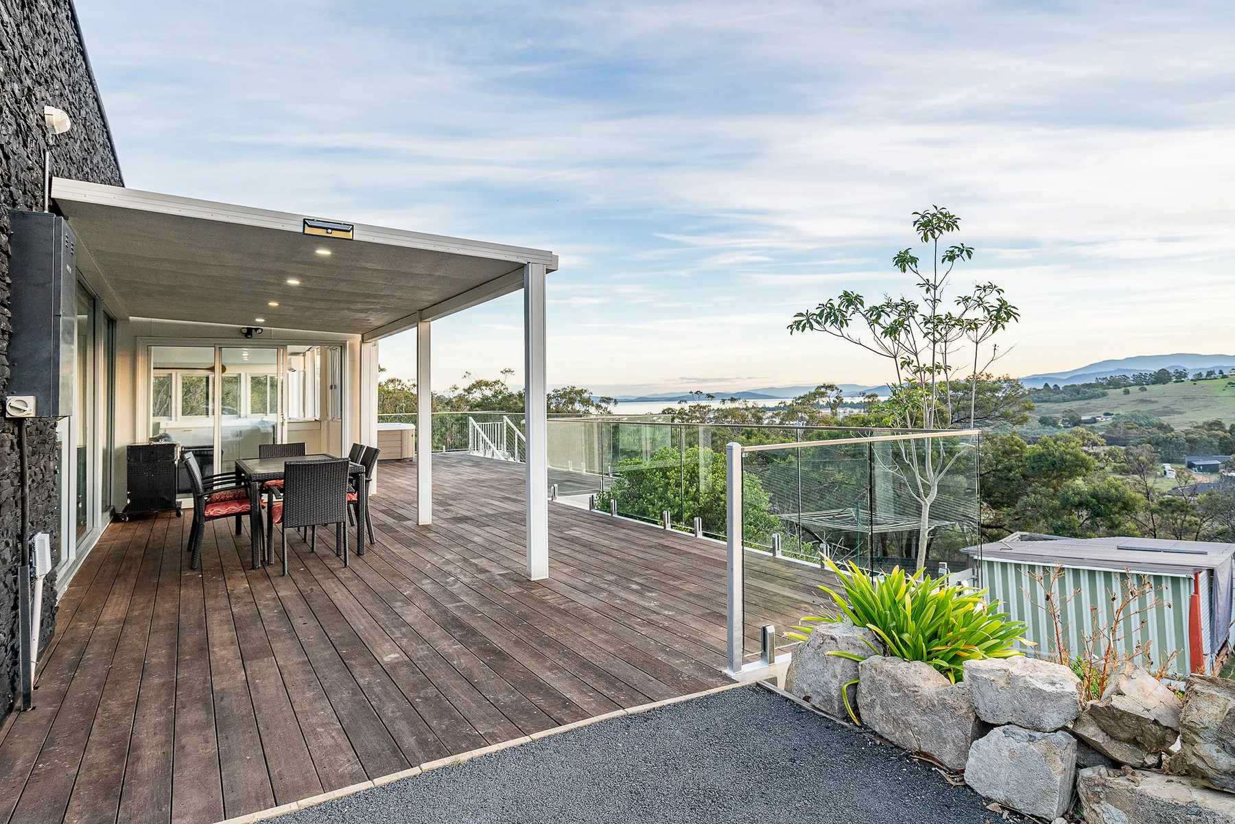 A covered outdoor deck has a dining table and seating overlooking the surrounding landscape.