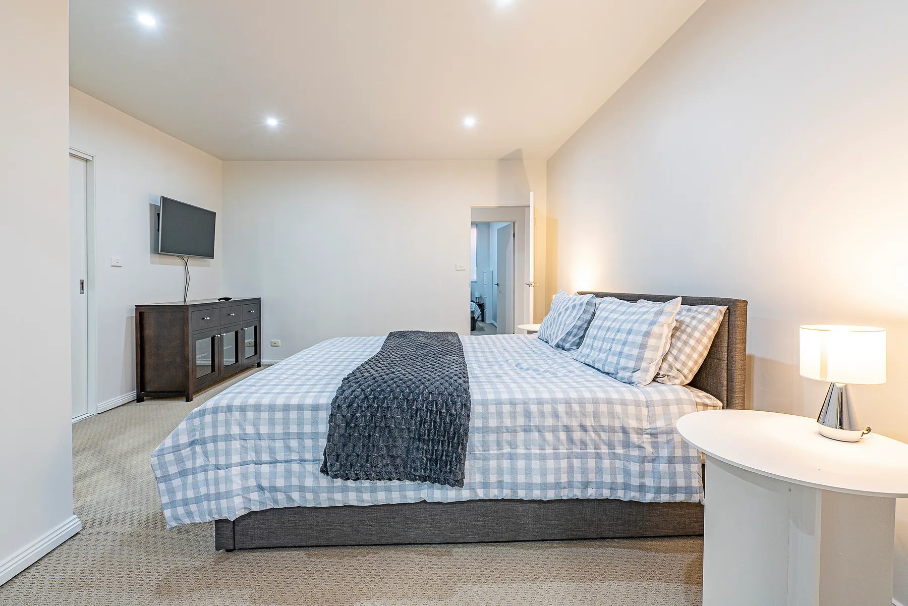 A bedroom with a large bed, a wall-mounted television, and a bedside table.