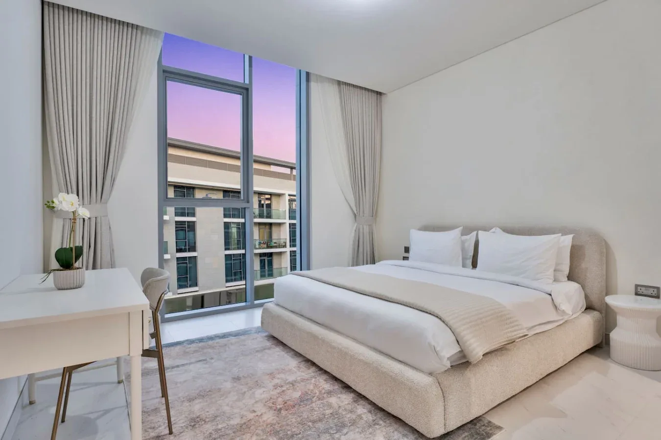 Un dormitorio luminoso con una cama grande junto a ventanales.