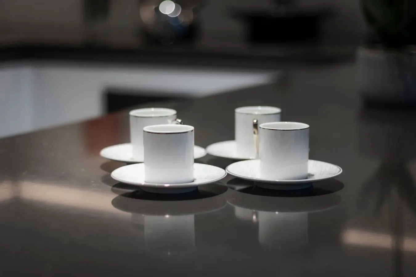 Comedor con tazas y platillos blancos sobre una mesa reflectante.