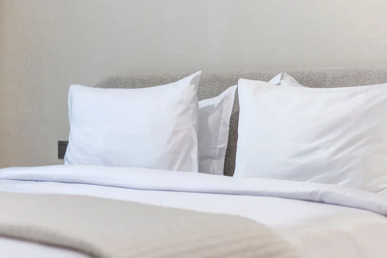 Una cama con ropa de cama blanca y almohadas junto a una pared lisa.