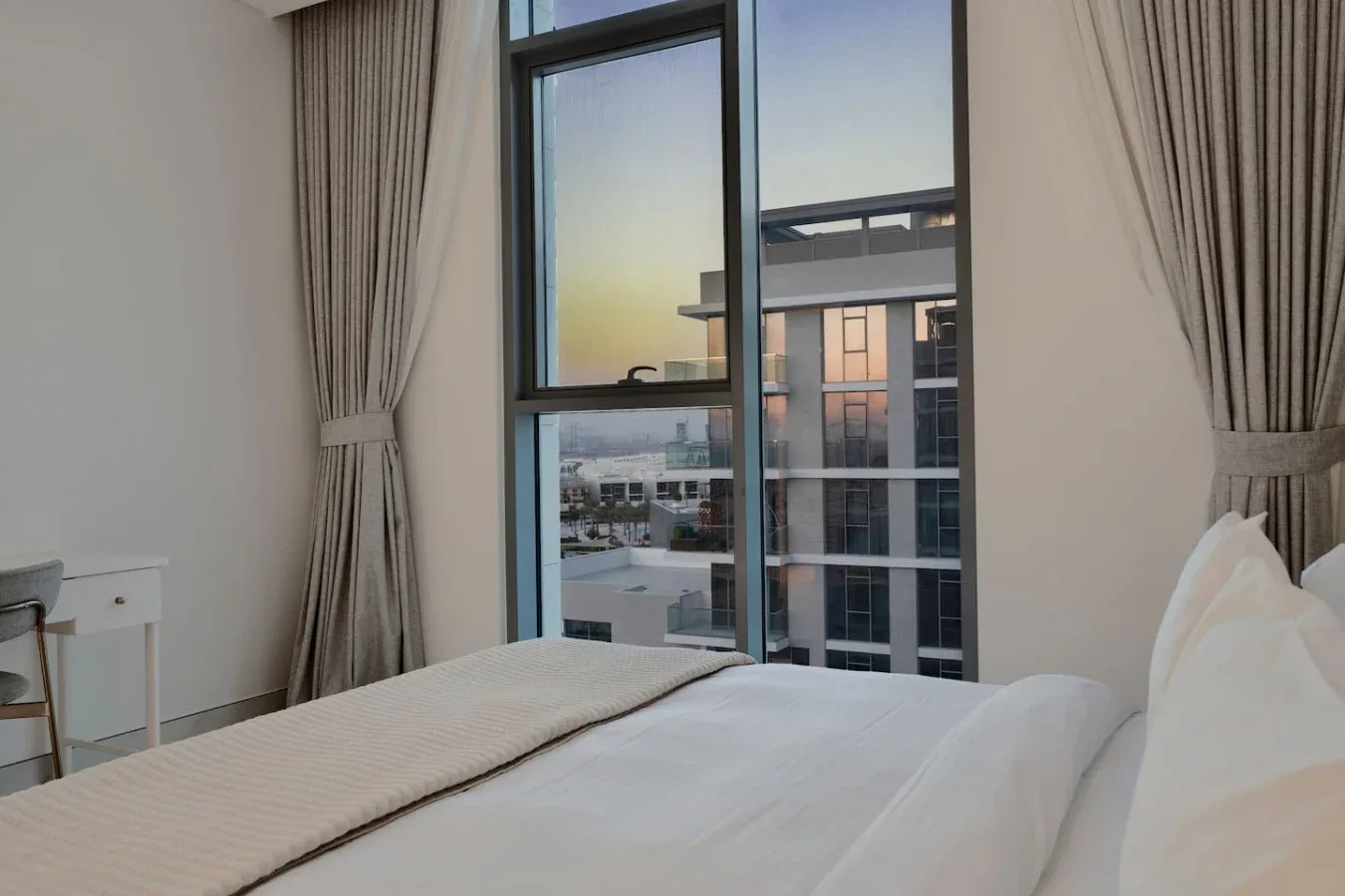 Dormitorio con una ventana grande con vista a edificios cercanos.
