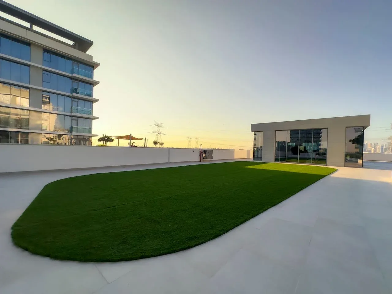 Una terraza en la azotea con un amplio césped verde junto a un edificio moderno con fachada de vidrio.