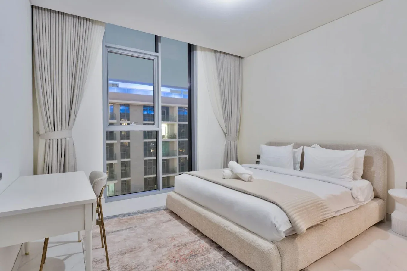 Un dormitorio con una cama junto a una ventana grande y cortinas claras.