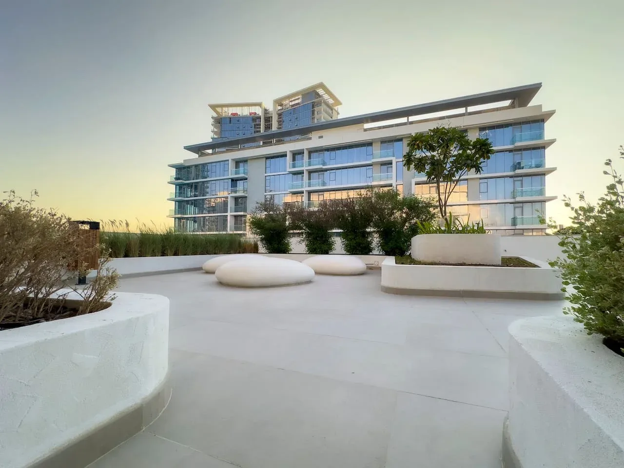 Terraza exterior junto a un edificio moderno con fachada de vidrio y zonas ajardinadas.