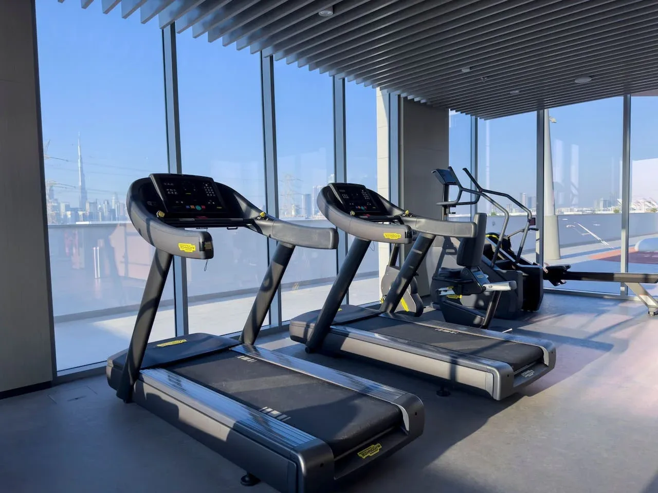 Sala de ejercicio con cintas de correr junto a grandes ventanales.