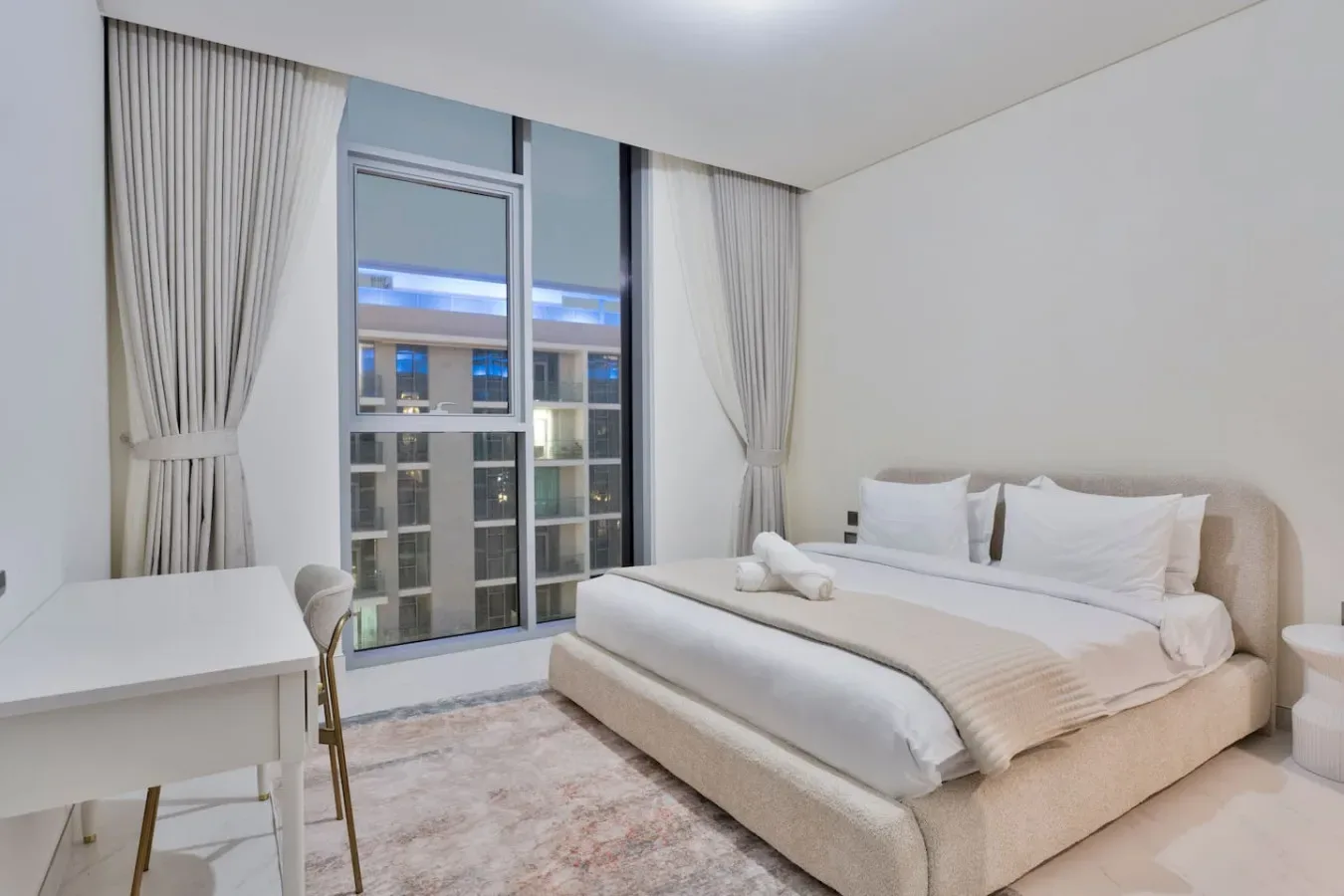 Un dormitorio con una cama junto a una ventana alta y cortinas claras.