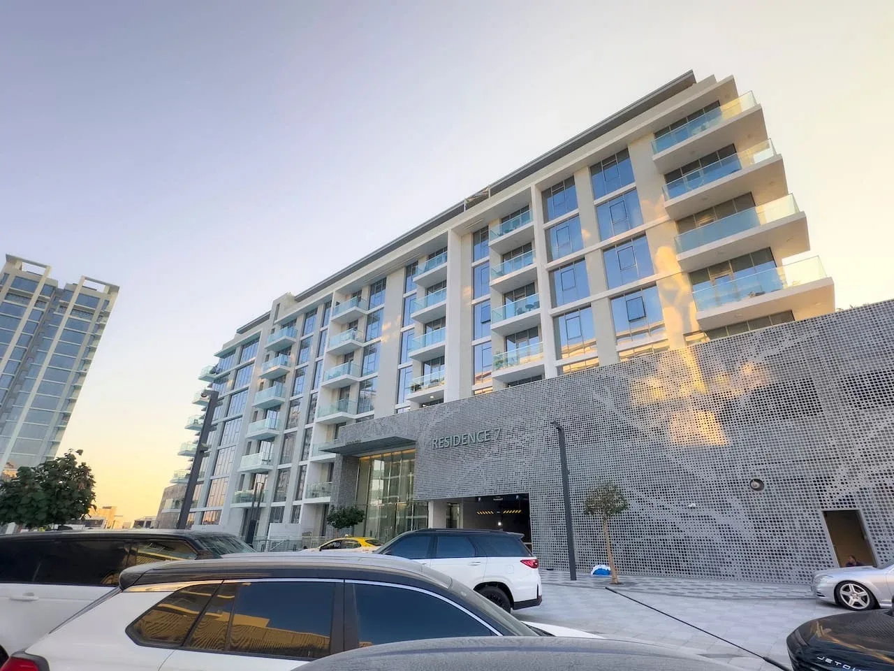 Vista exterior de un edificio de apartamentos moderno con vehículos estacionados delante.