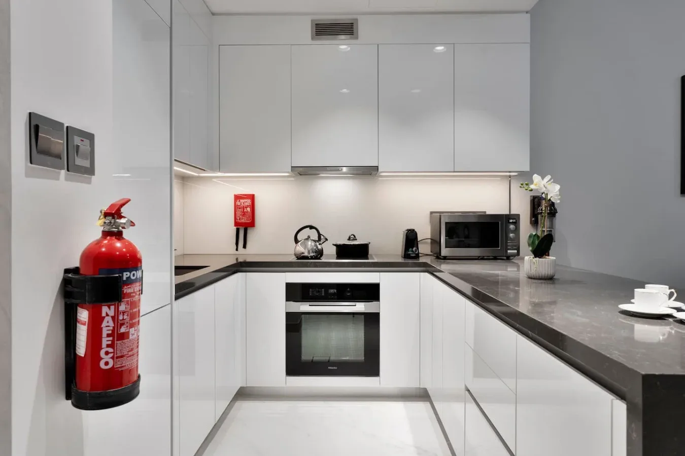 Una cocina moderna con armarios blancos, encimeras oscuras y electrodomésticos integrados.