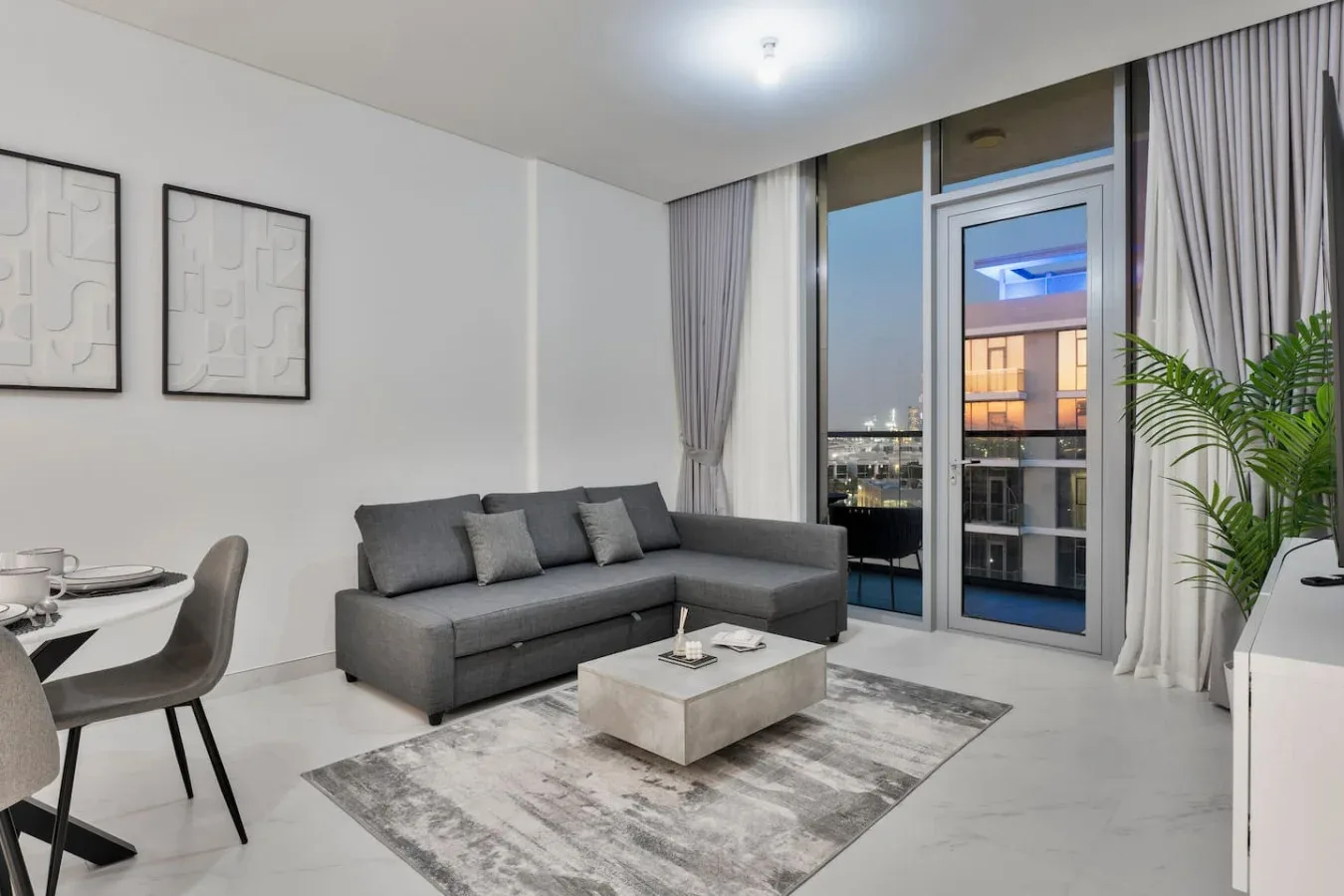 Sala de estar con asientos grises, una mesa de centro y ventanas con vistas a edificios cercanos.