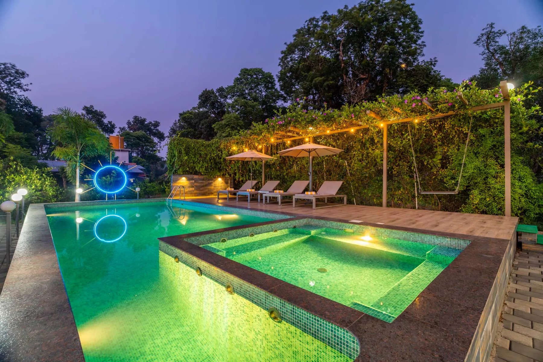 Una piscina exterior brilla bajo luces decorativas, con asientos junto al agua.