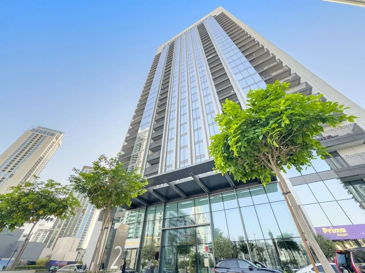 A modern high-rise building rises above a glass-fronted ground floor and street trees.