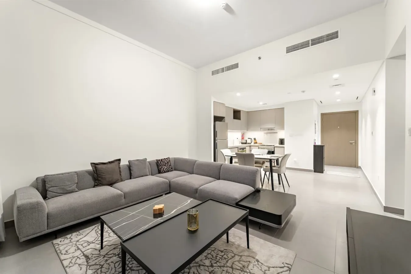 A bright living room with gray seating and an open kitchen in the background.