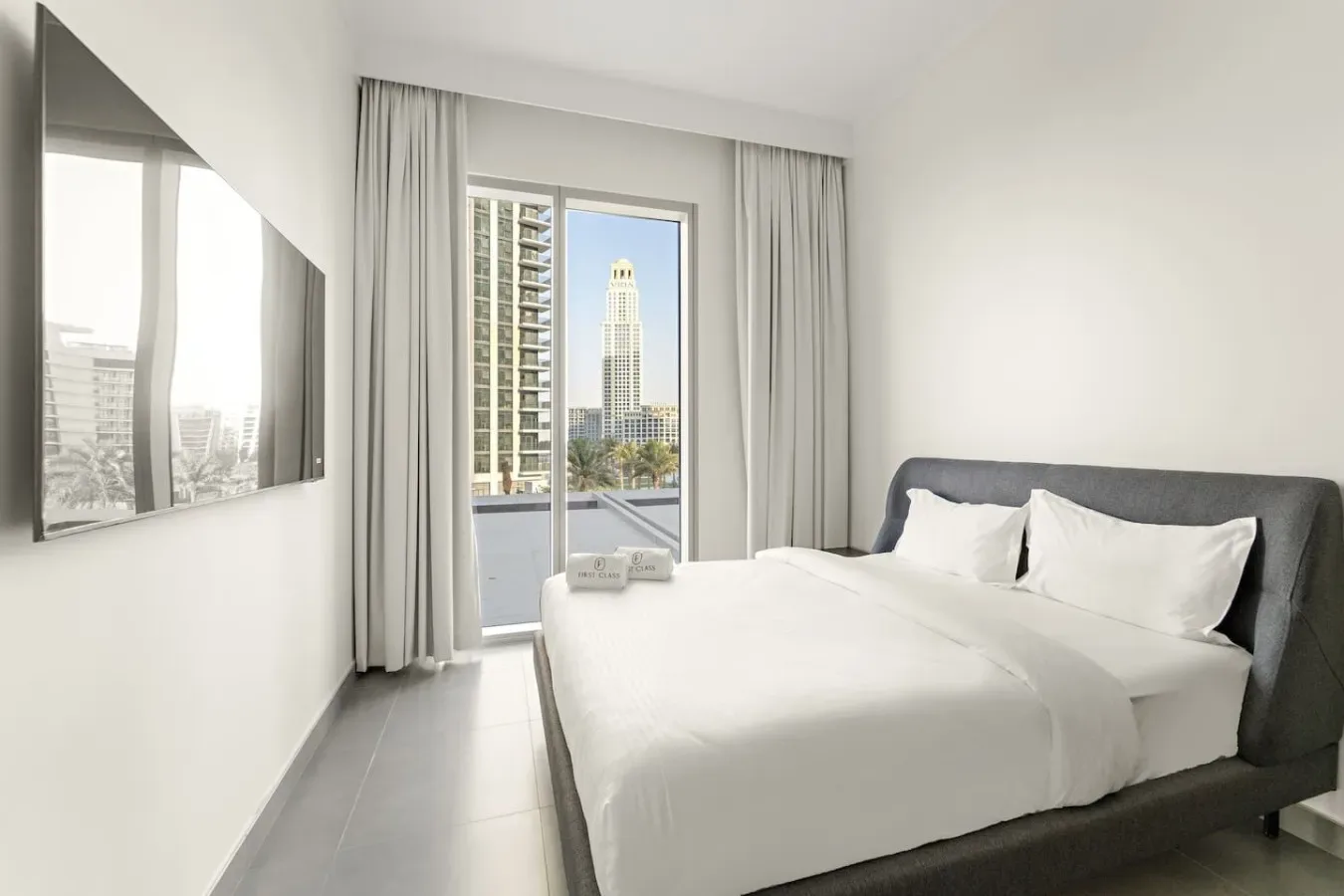 A bright bedroom with a neatly made bed beside a large window.