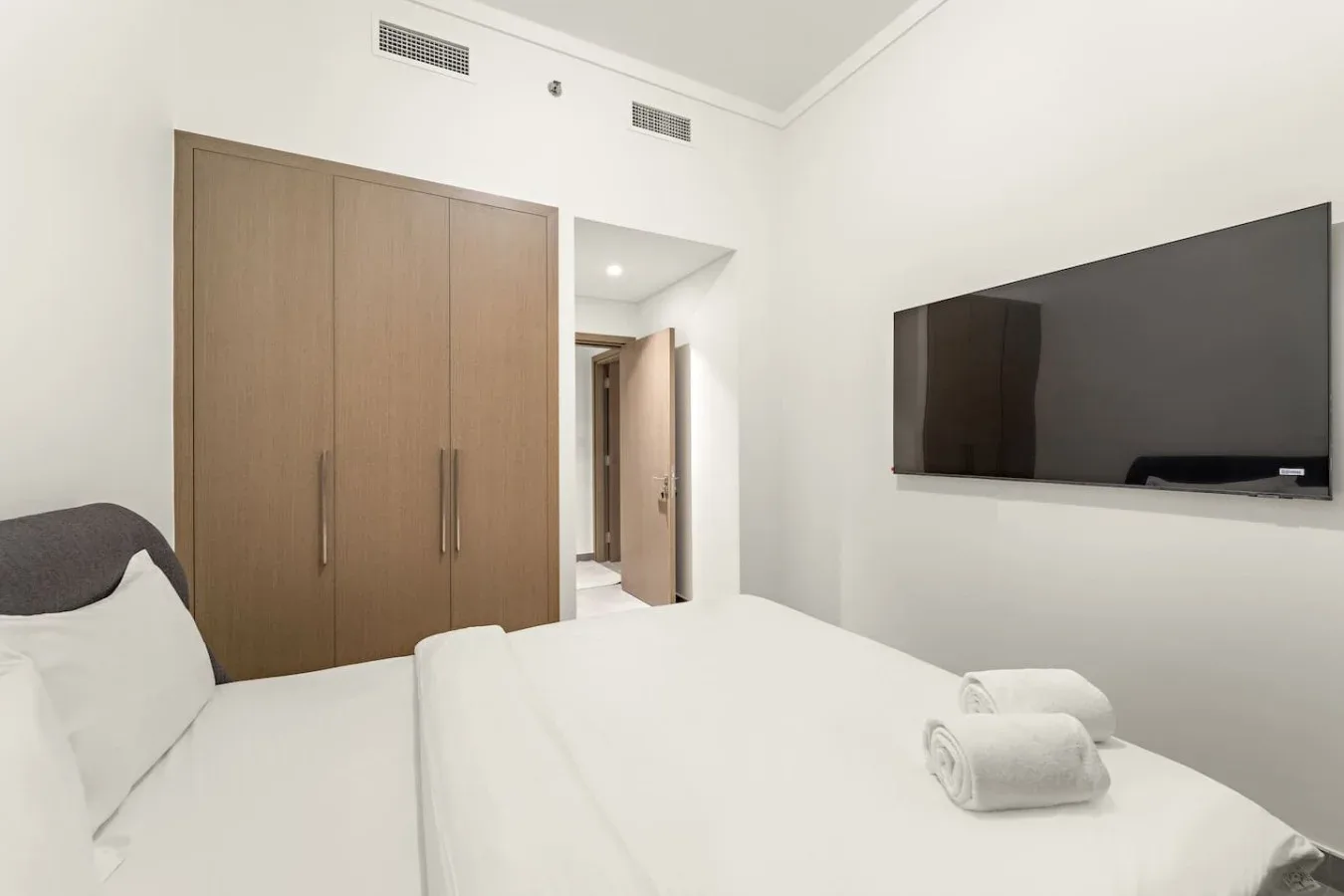 A bright bedroom with a neatly made bed, wardrobe, and wall-mounted television.