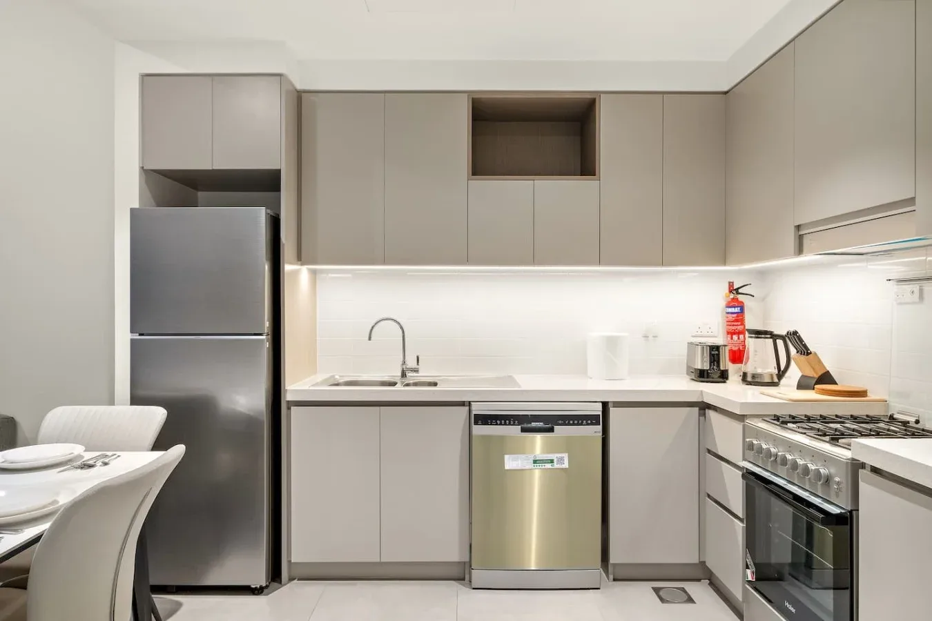 A modern kitchen with pale cabinets, a refrigerator, and stainless steel appliances.