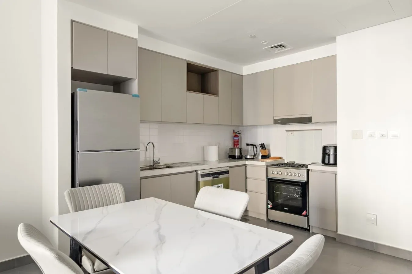 A modern kitchen with pale cabinetry and a dining table in the foreground.