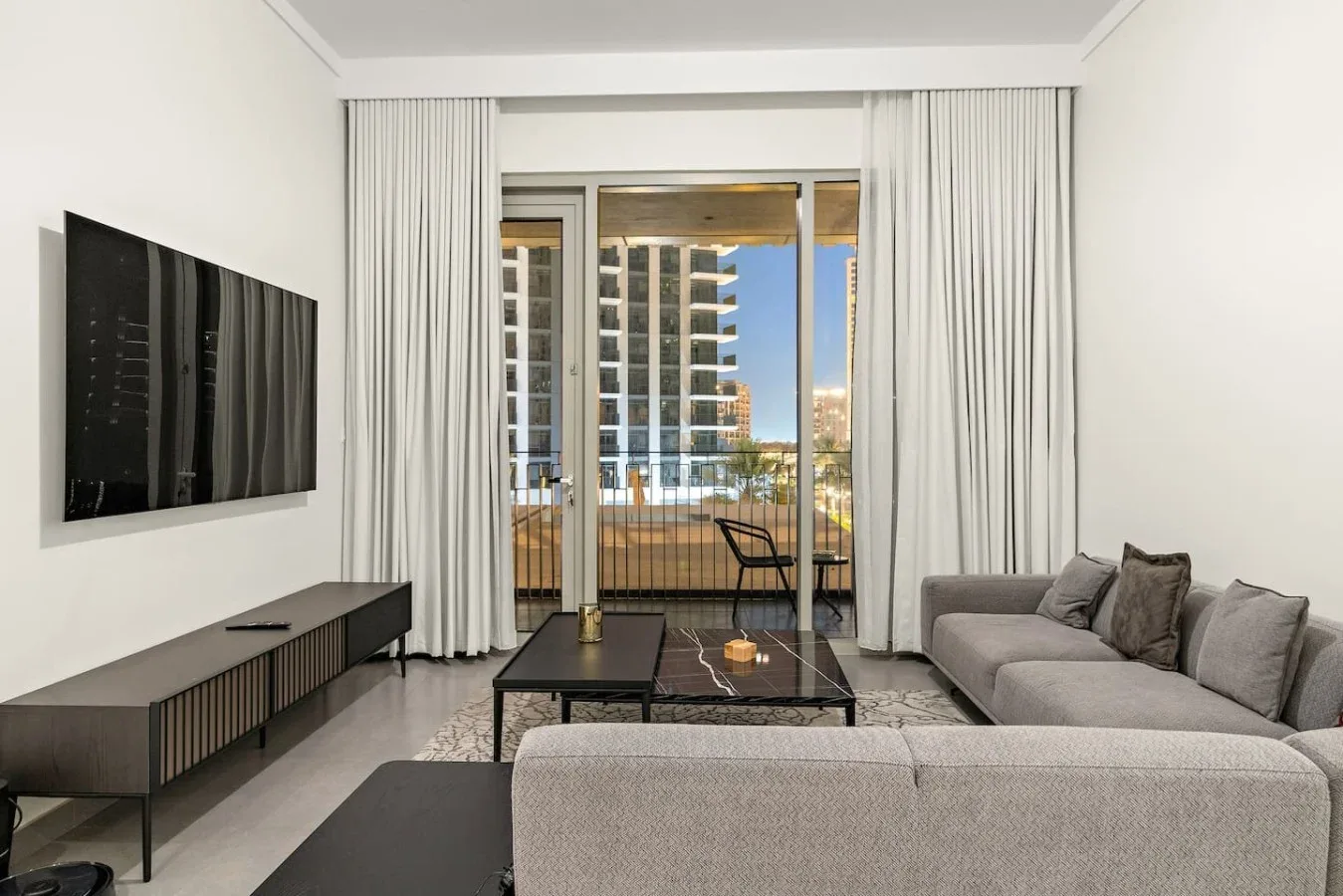 A living room with seating, a television, and glass doors opening onto a balcony.