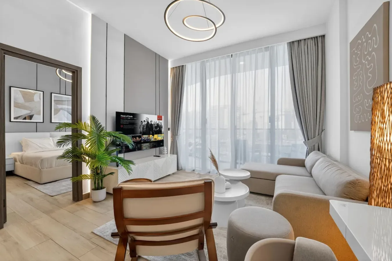 Luminoso salón con asientos, un televisor y grandes ventanas con cortinas.