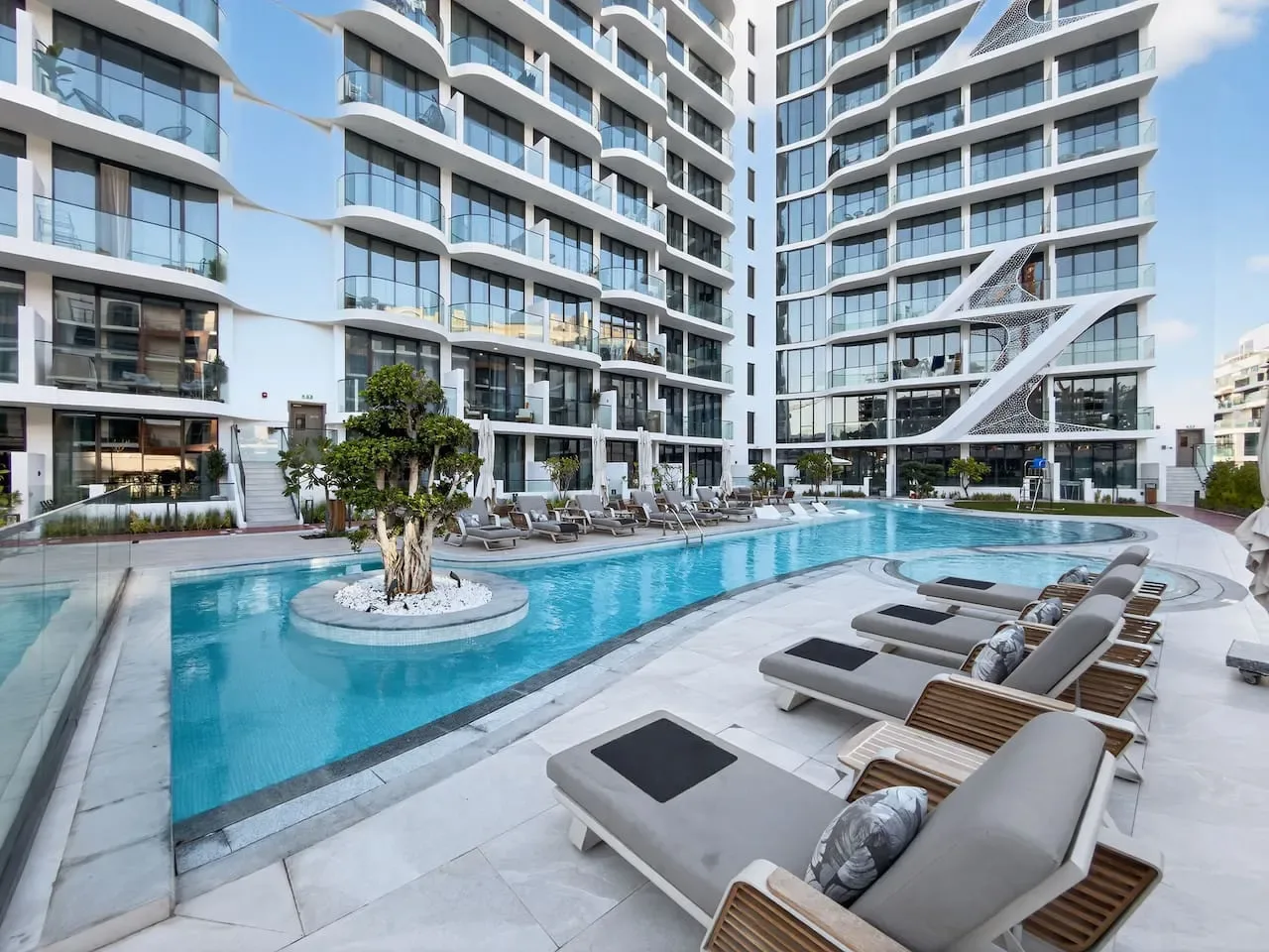 Una piscina al aire libre con asientos de descanso junto a edificios modernos de gran altura.
