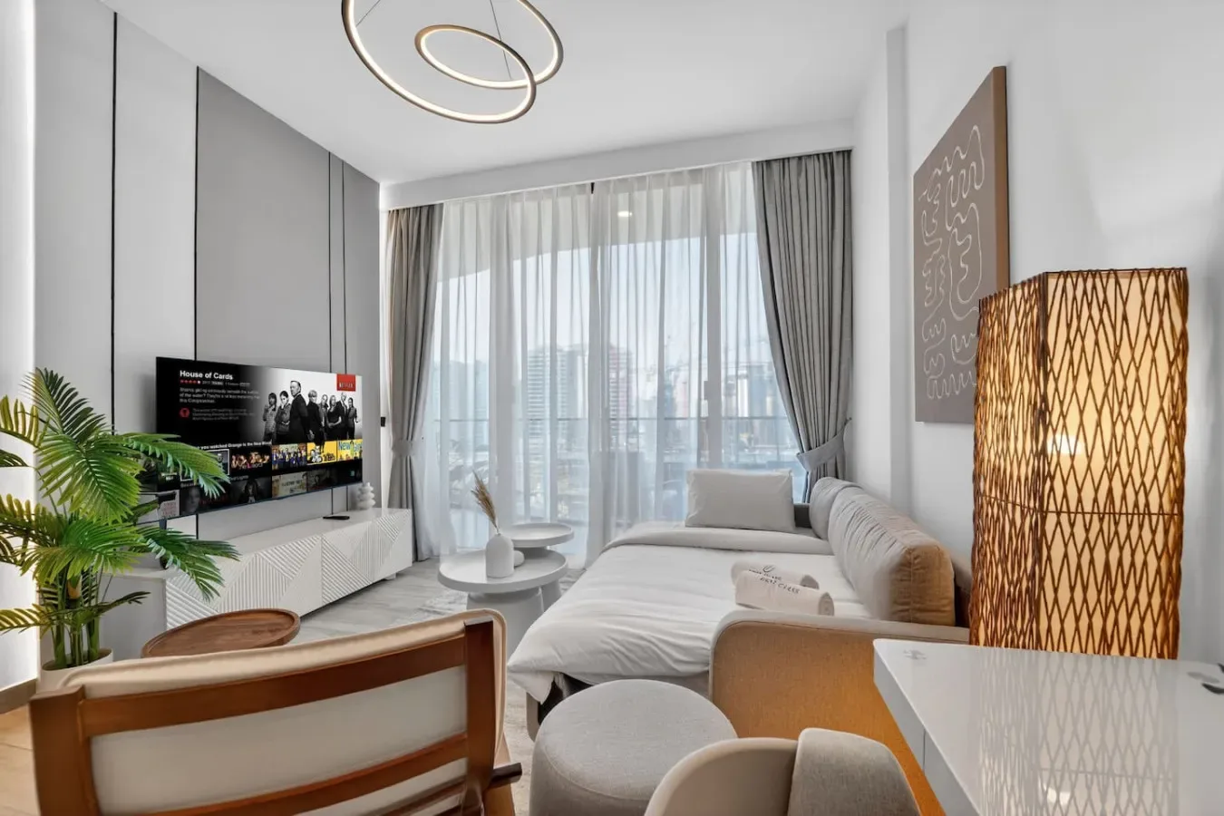 Una sala luminosa con asientos, un televisor y grandes ventanas con cortinas.