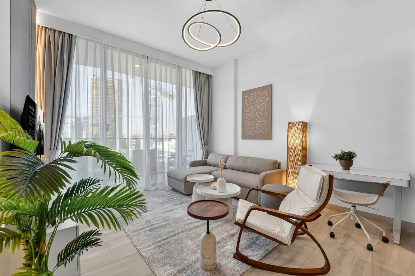 Una sala luminosa con asientos, una mesa de centro y grandes ventanales con cortinas.