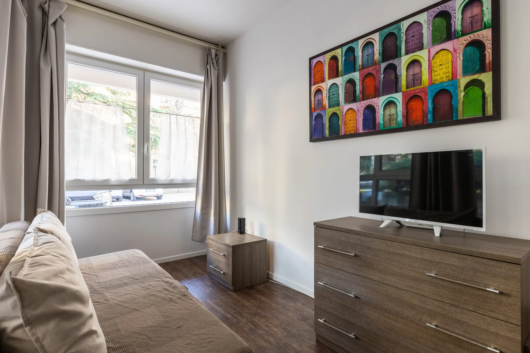Un dormitorio con una cama, una ventana y un televisor sobre una cómoda.