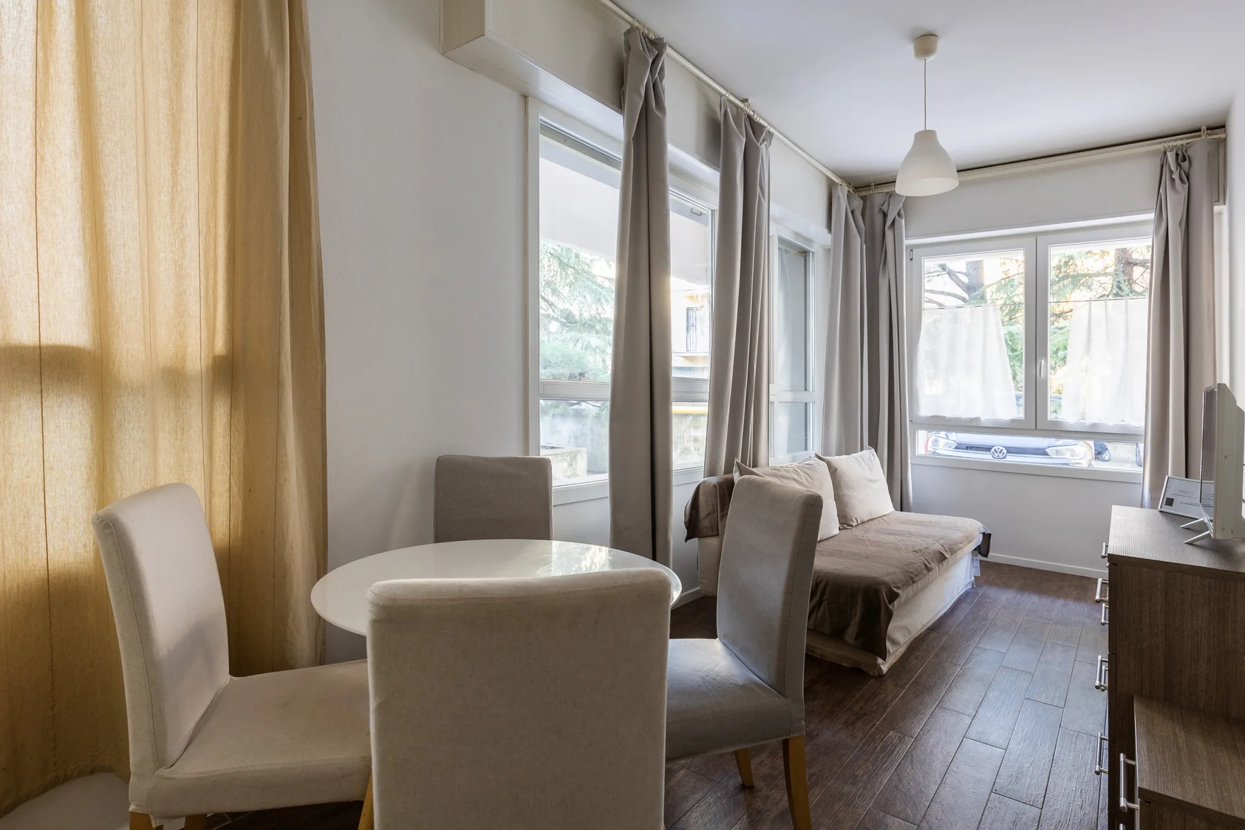 Una sala luminosa con mesa de comedor, asientos y grandes ventanas.