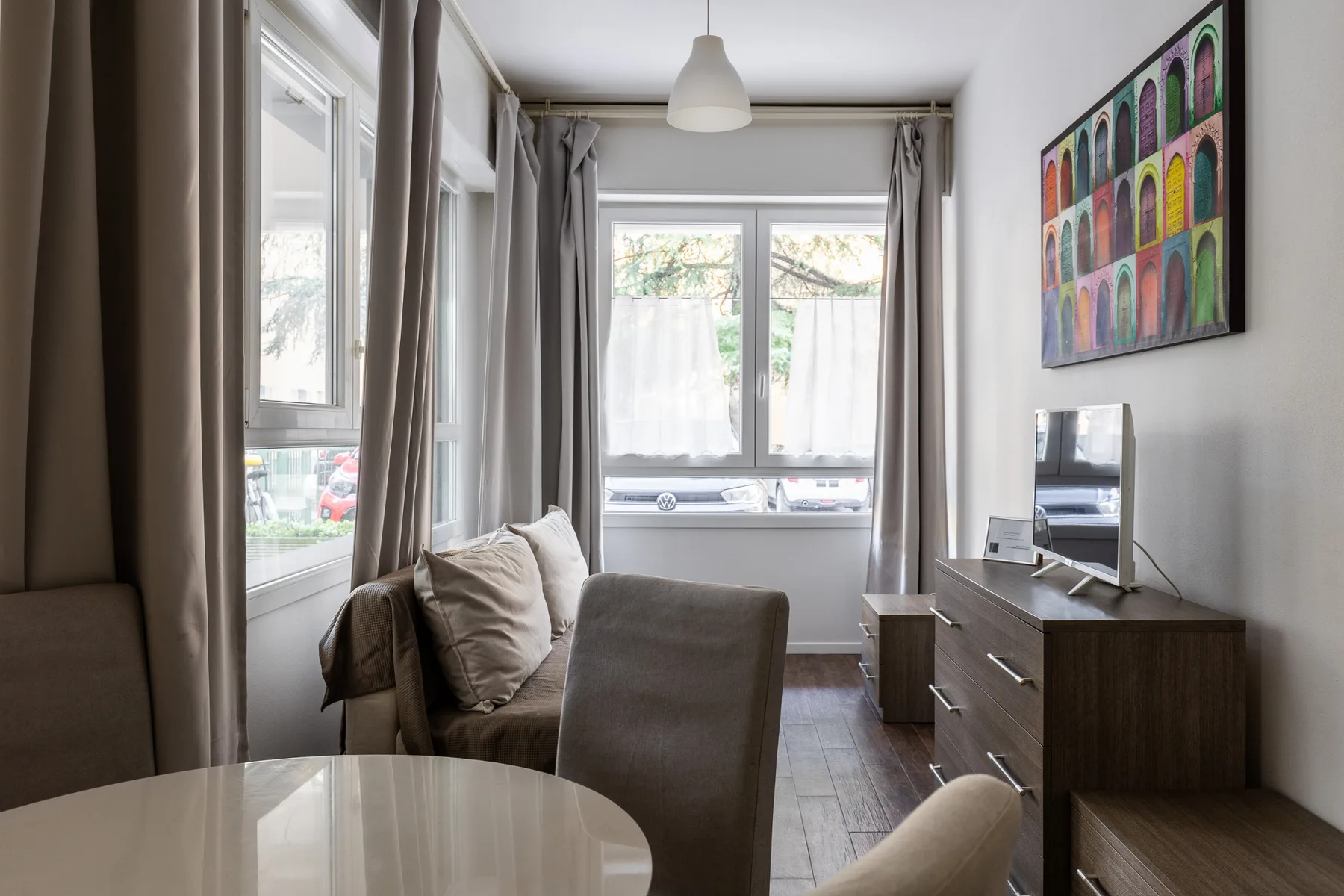 Una sala de estar luminosa con sofá, mesa redonda y escritorio junto a las ventanas.
