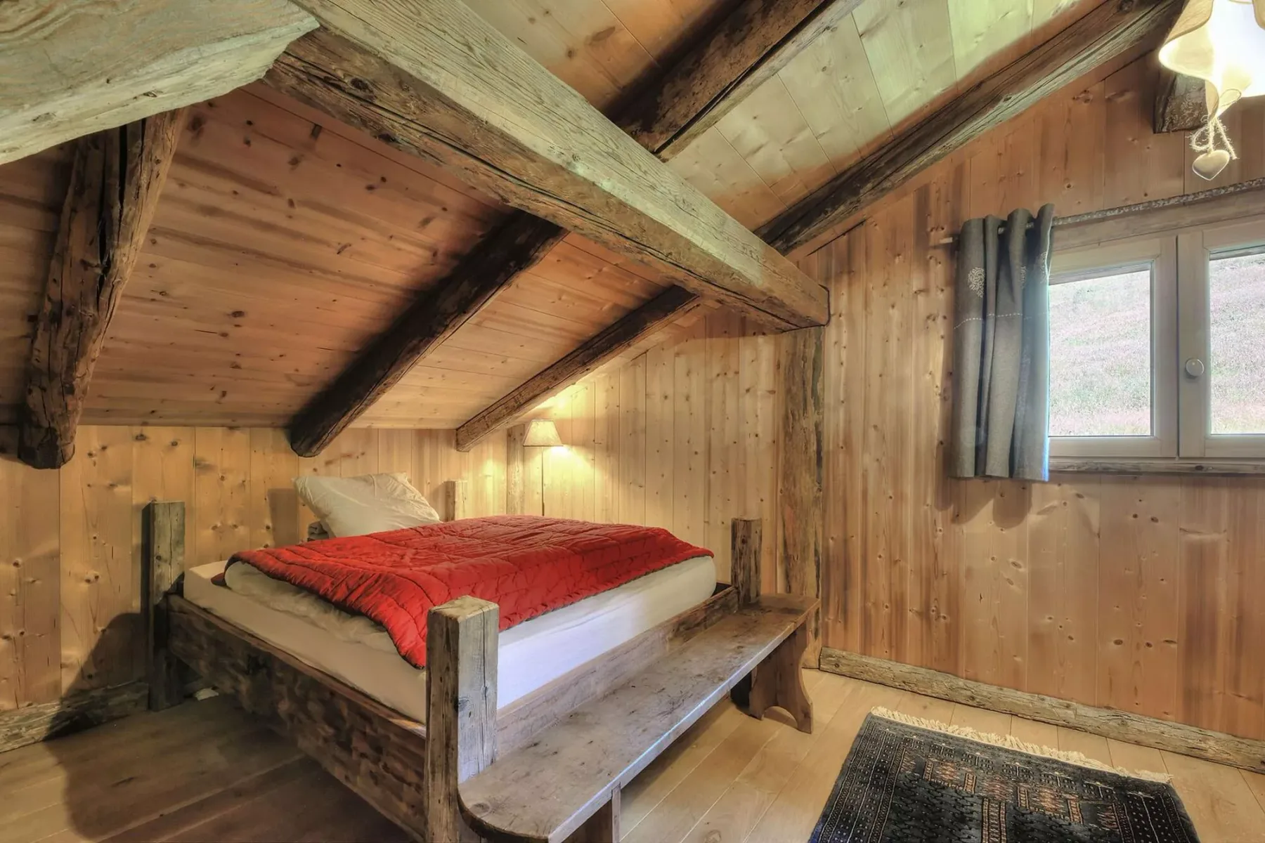 A wood-paneled bedroom with a bed covered by a red blanket.