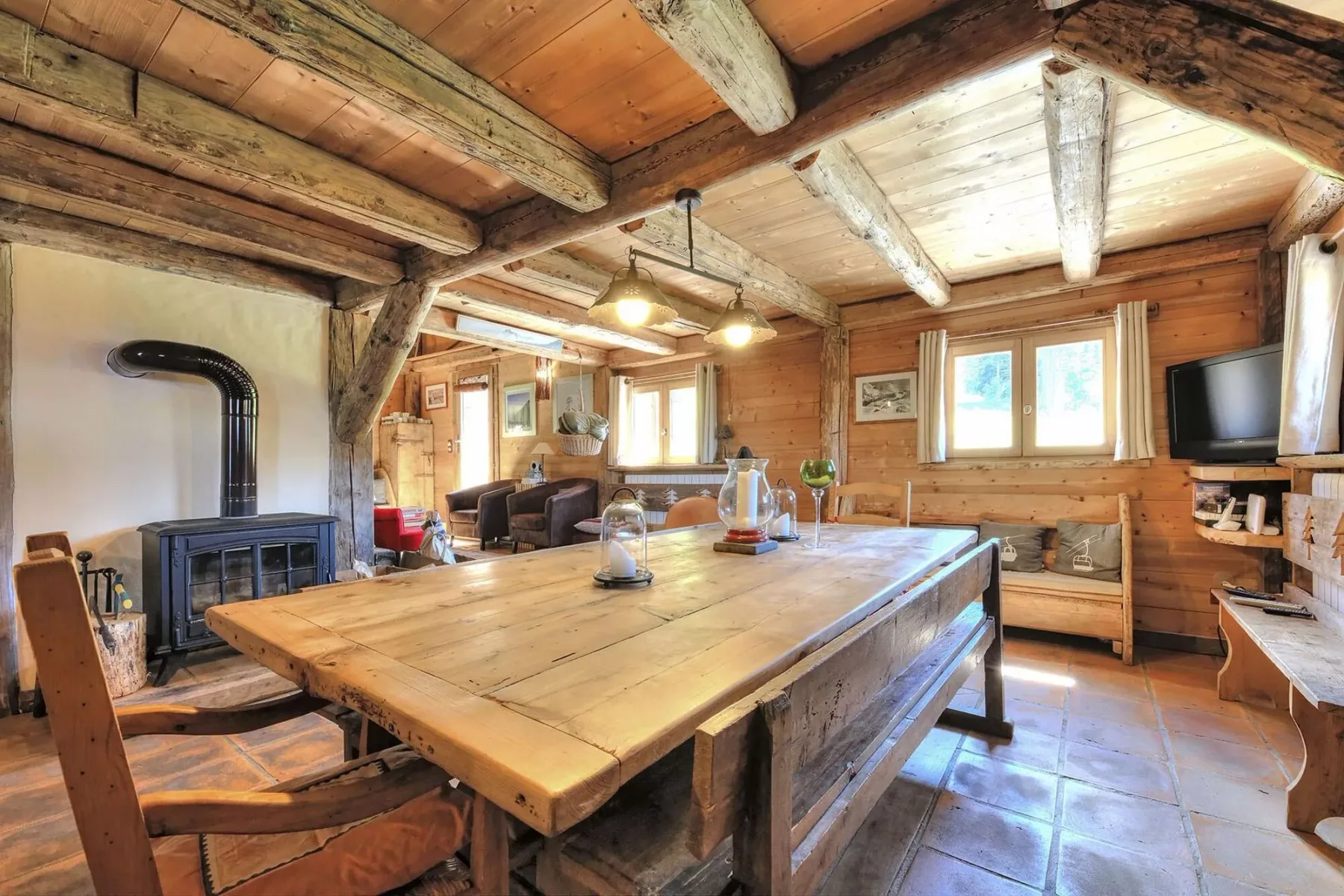 A rustic dining area has a large wooden table and a wood-burning stove.