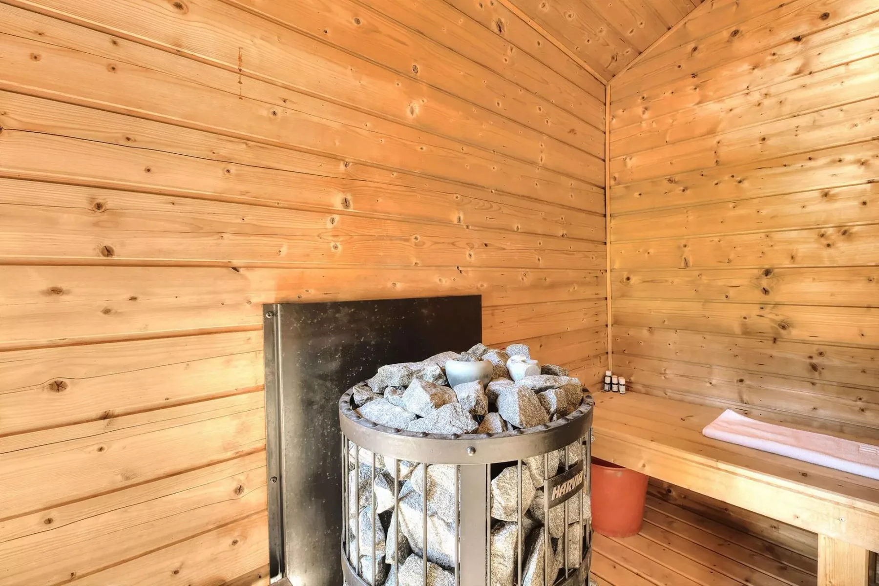 A wood-paneled sauna room with a stone-filled heater and built-in bench.
