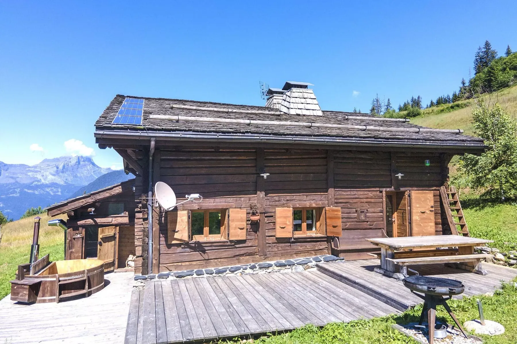 A wooden chalet with a broad deck and mountain scenery in the background.