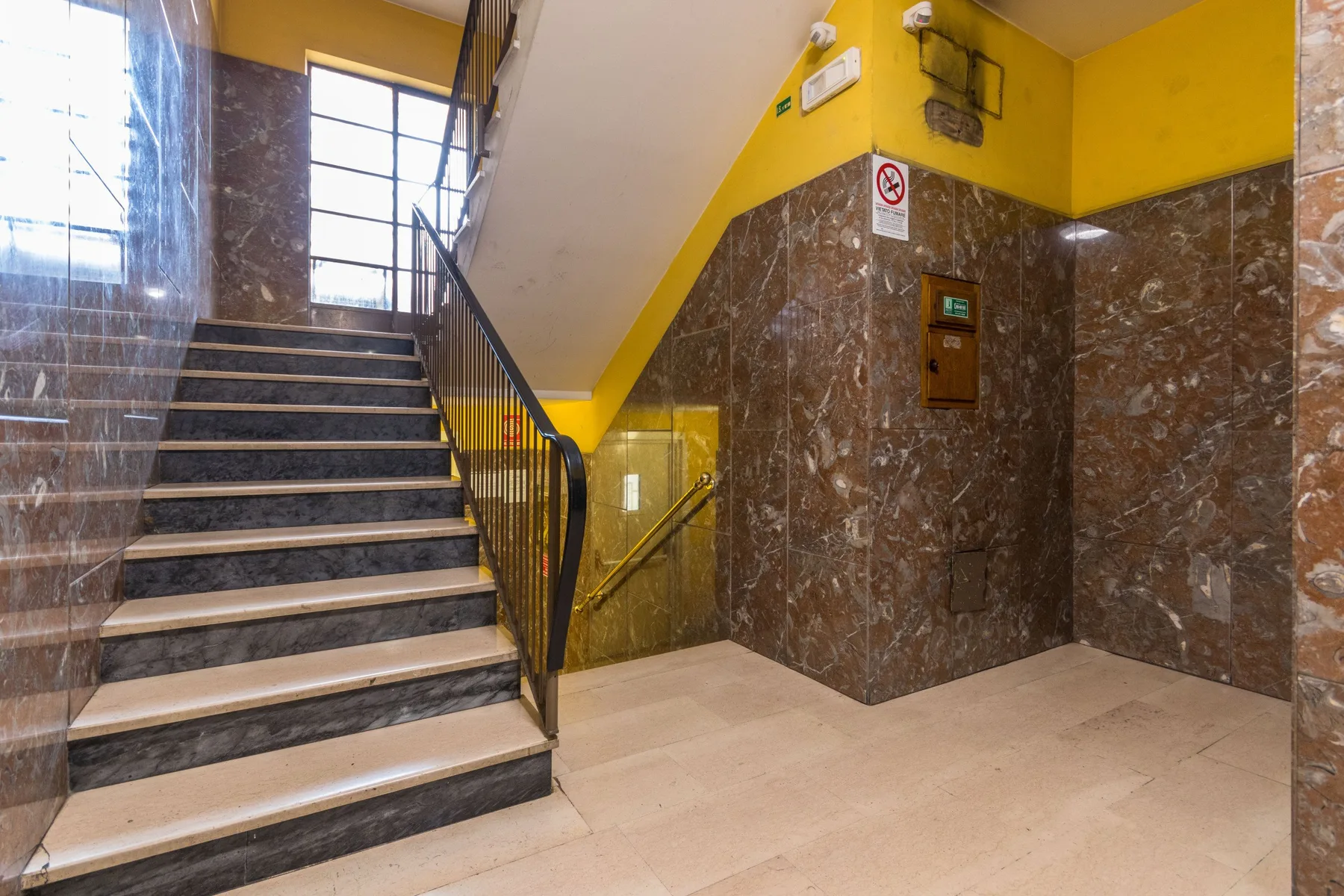 Una escalera con barandilla oscura y paredes amarillas en la parte superior.