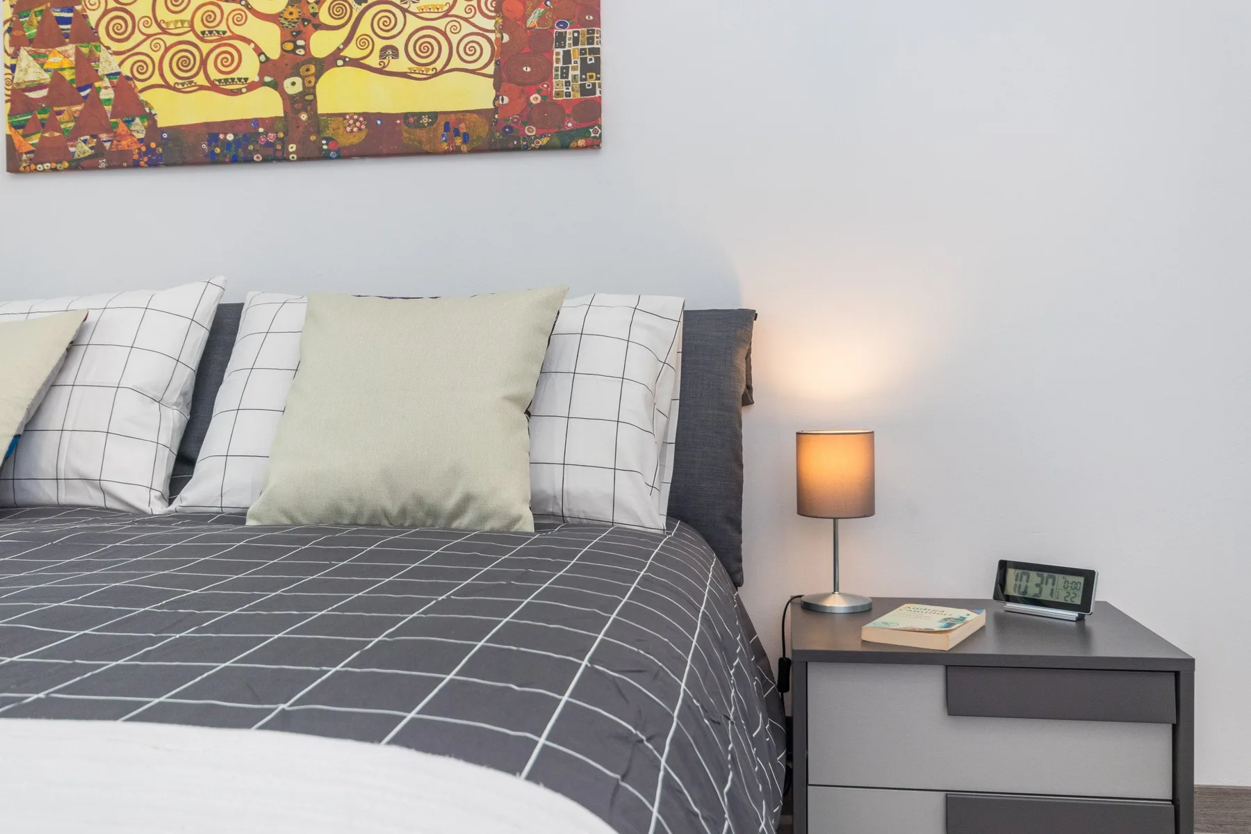Un dormitorio con una cama bien tendida y una mesita de noche con una lámpara.