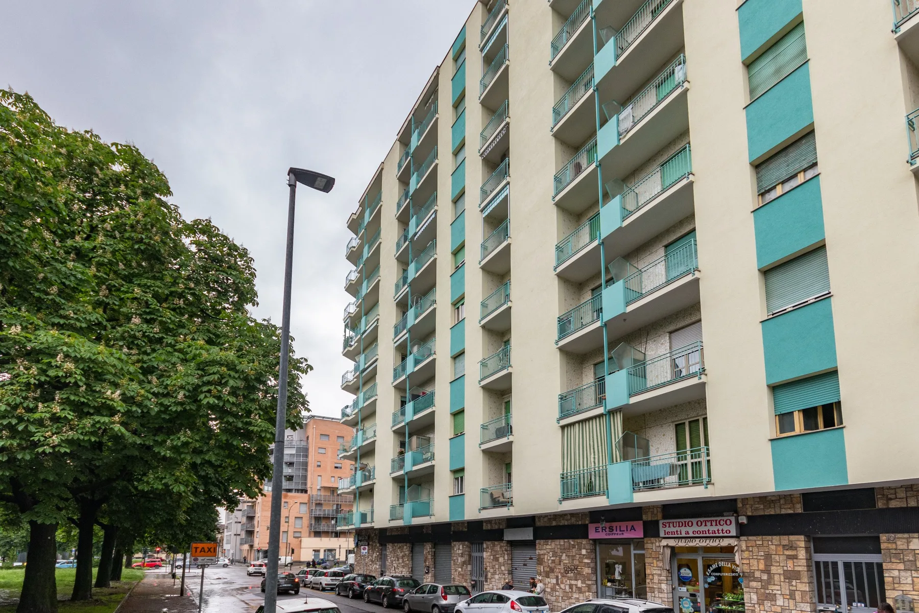 Un edificio de apartamentos de varios pisos con balcones se alza junto a una calle arbolada.